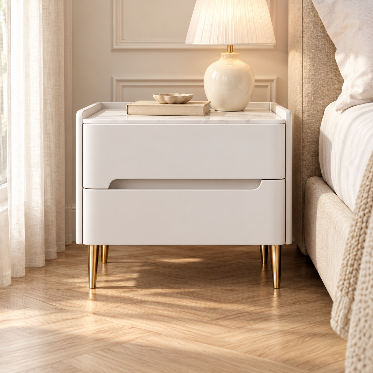 Table de chevet blanche avec une lampe et un livre près d’un lit beige, dans une chambre avec moulures et parquet clair