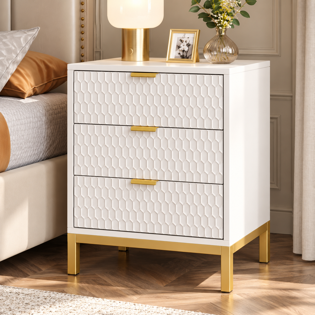 Table de chevet blanche et dorée à côté d’un lit beige, avec moulures crème et parquet clair en chevrons.