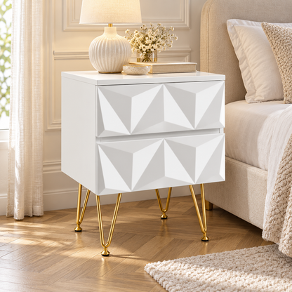 Chevet blanc à deux tiroirs en relief près d’un lit beige, avec lampe, moulures et parquet clair en chevrons