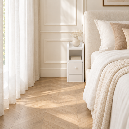 Même chambre aménagée avec un chevet blanc étroit près du lit, un vase fleuri et des livres dans la niche.