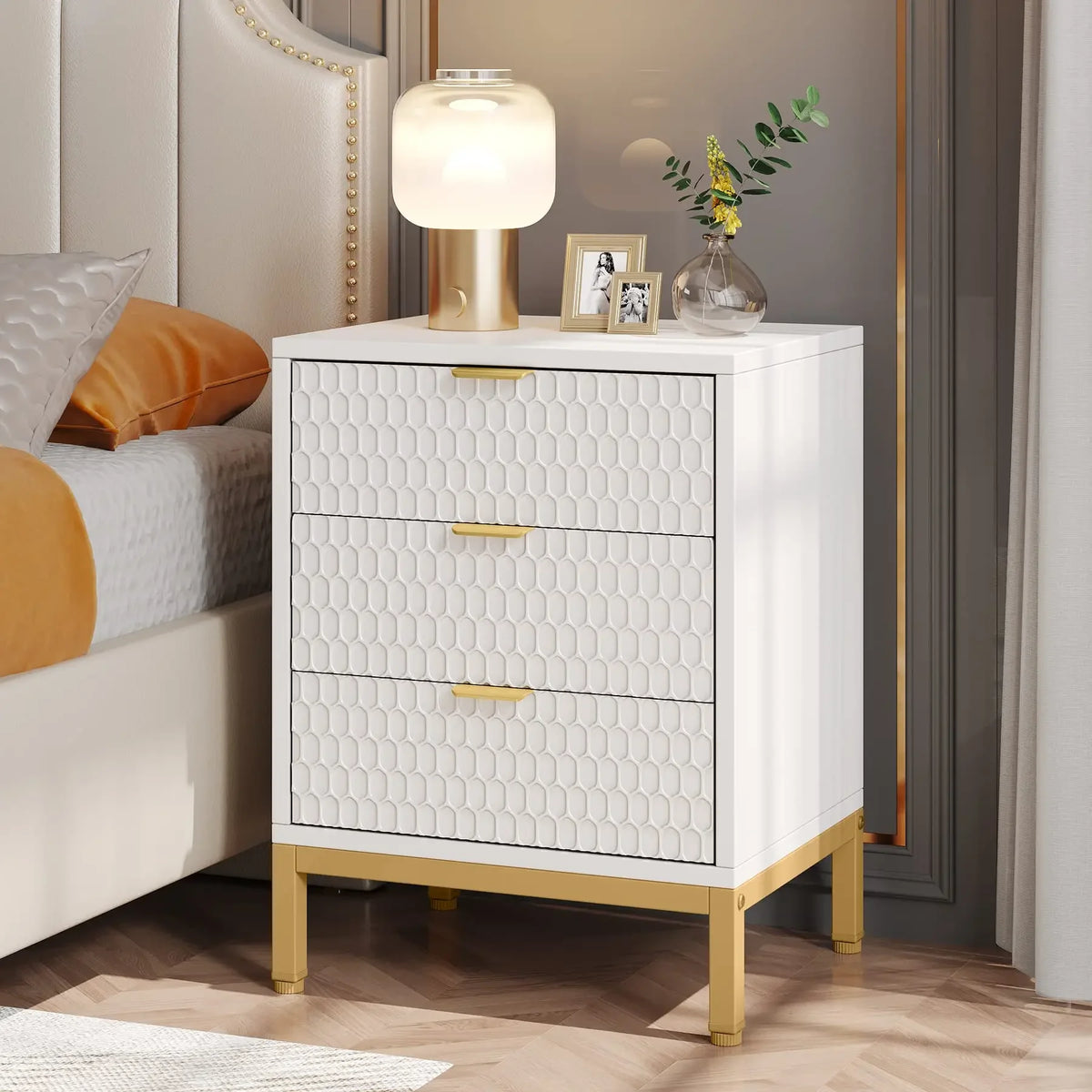 Table de chevet blanche et dorée avec une lampe et un vase dans une chambre lumineuse aux moulures crème.