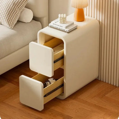 Table de chevet étroite crème avec deux tiroirs ouverts et des lignes arrondies 