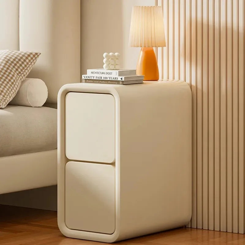 Table de chevet crème à deux tiroirs avec une lampe près d’un lit beige dans une chambre lumineuse