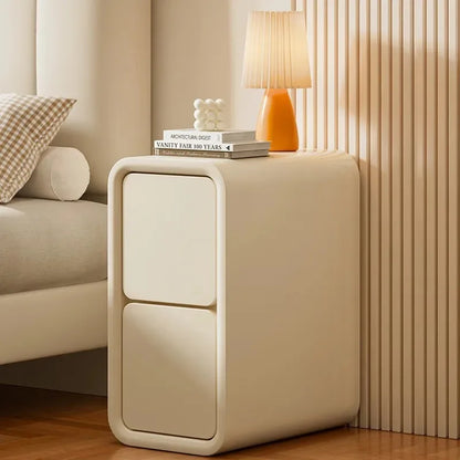 Table de chevet crème à deux tiroirs avec une lampe près d’un lit beige dans une chambre lumineuse