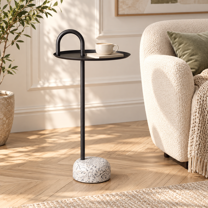 Table d’appoint noire avec une tasse et un livre près d’un fauteuil écru dans un coin lecture lumineux
