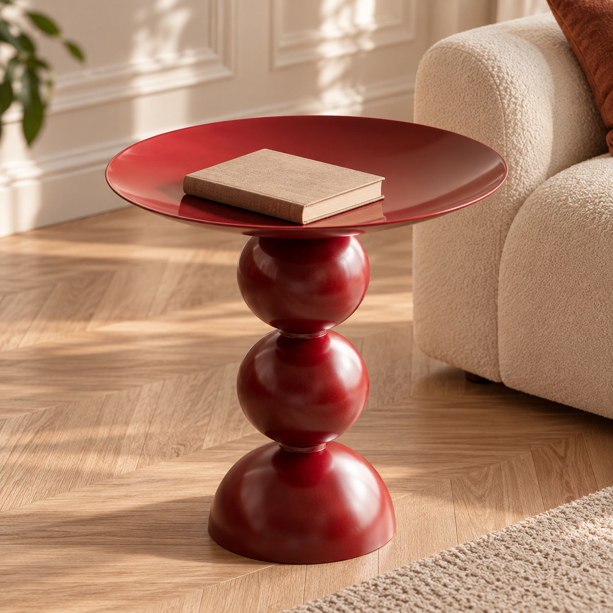 Table d’appoint rouge bordeaux avec un livre dans son plateau creusé près d’un fauteuil écru
